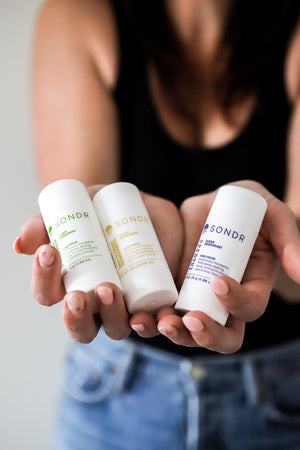 Women holding three travel size SONDR deodorants